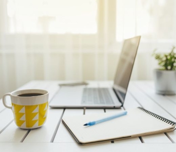A laptop on a desk with a cup of coffee